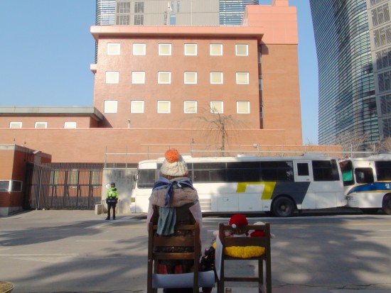 Japanese_Embassy_in_Seoul_and_watched_from_behind_a_bronze_statue_of_comfort_women